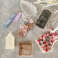 Gift Box NZ | New Zealand made products | Small gift boxes NZ | Gift in New Zealand |  A large size gift box jam packed with handmade products, all packaged in a pretty blue daisy fabric box. Leaf shaped trinket tray in white. Large white soy wax blend Home candle. Set of two produce bags.